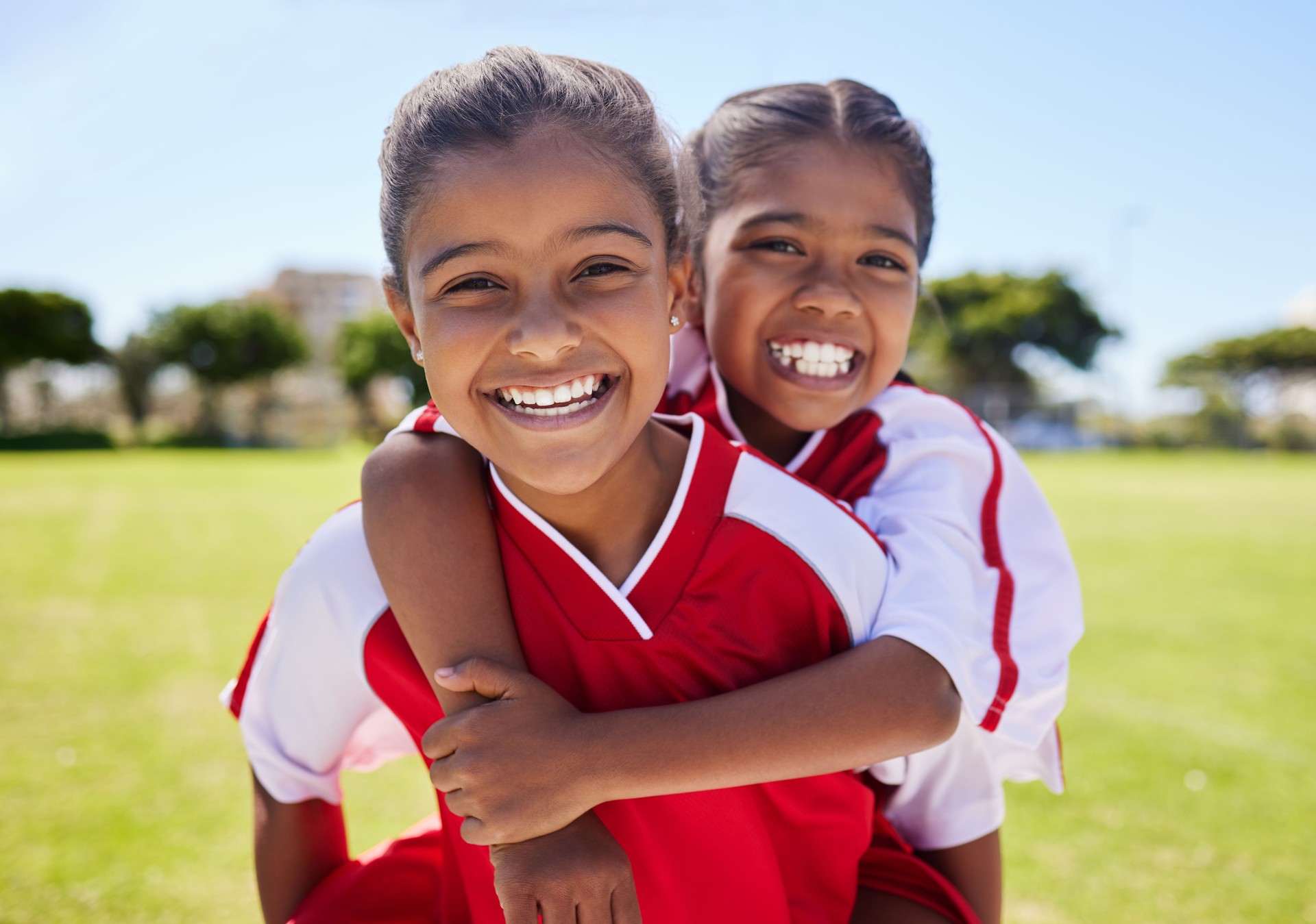 Girl, friends and portrait smile on football field having fun before training for match, game or competition. Soccer pitch, sports and kids piggy back on grass learning sports for fitness exercise.